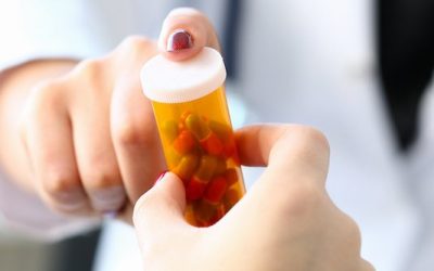 Female medicine doctor hand hold jar of pills and write prescription to patient at worktable. Panacea and life save prescribing treatment legal drug store concept.