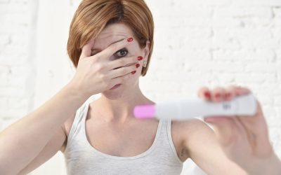 young pregnant woman  holding pink positive pregnancy test covering her eyes with her hand scared about a negative result in fertility and motherhood concept