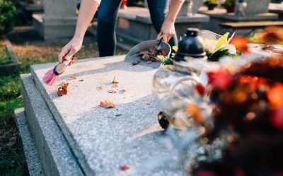 A woman cleans the grave. Sweeps leaves from the tombstone. Preparations for All Saints Day on November 1