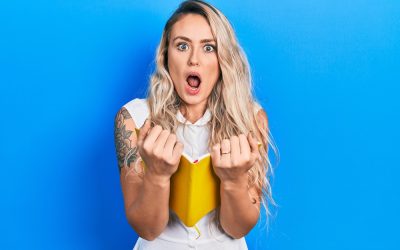 Beautiful young blonde woman reading a book afraid and shocked with surprise and amazed expression, fear and excited face.