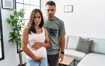 Young interracial couple expecting a baby, touching pregnant belly skeptic and nervous, frowning upset because of problem. negative person.