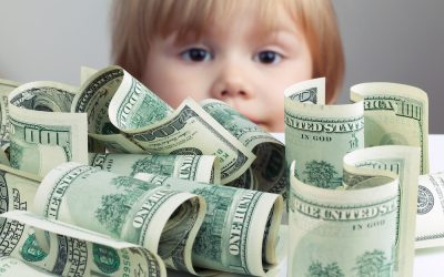 Pile of United States dollar hundred USD banknotes on white table and blurred baby looking on it on a background. Retro tonal correction photo filter effect, selective focus on money