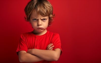 studio portrait of a very angry and petulant child in a red shirt. arms folded. exaggerating and feigning anger