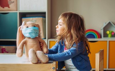 Little girl playing with rabbit soft toy in the medicine mask sitting at the table in the kids room.